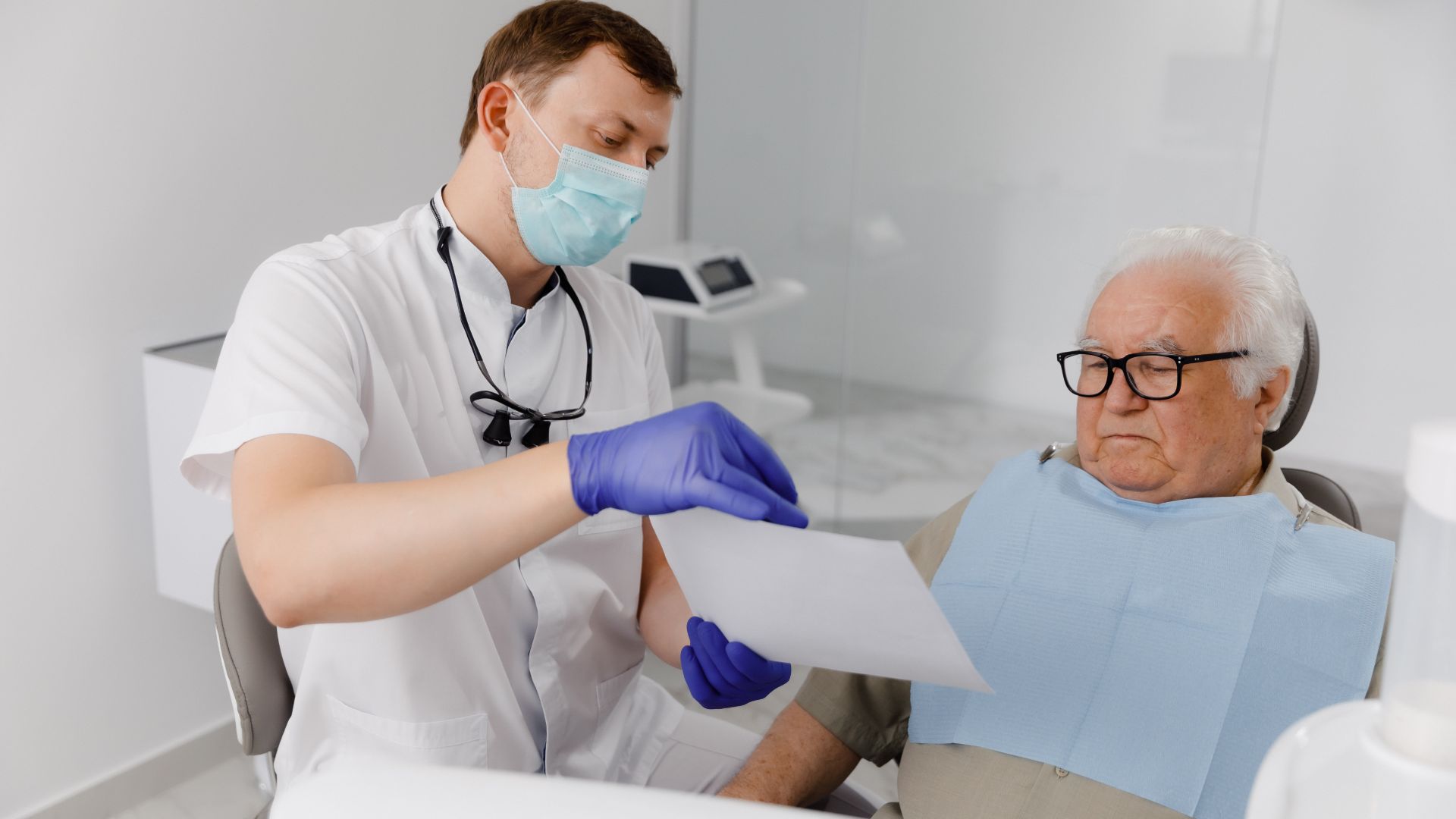 Fogorvos a fogorvosi székben ülő idős úrnak ad felvilágosítást